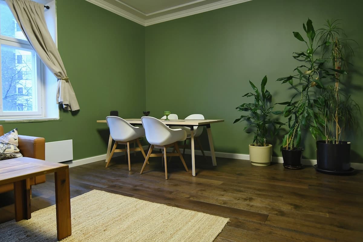 Dining area with white chairs, oak table, and green walls with plants